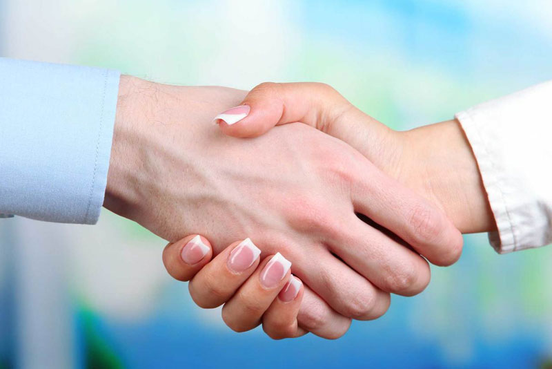 Two people shaking hands in front of a blue background.