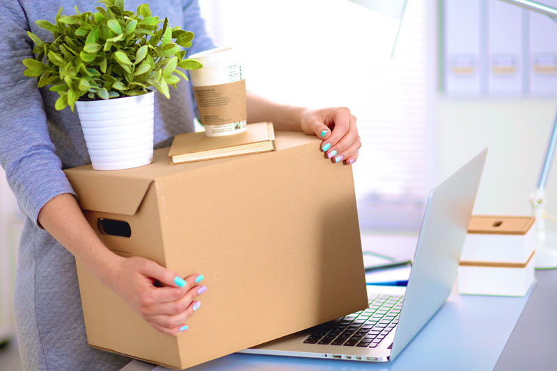 A woman holding a cardboard box and a laptop.