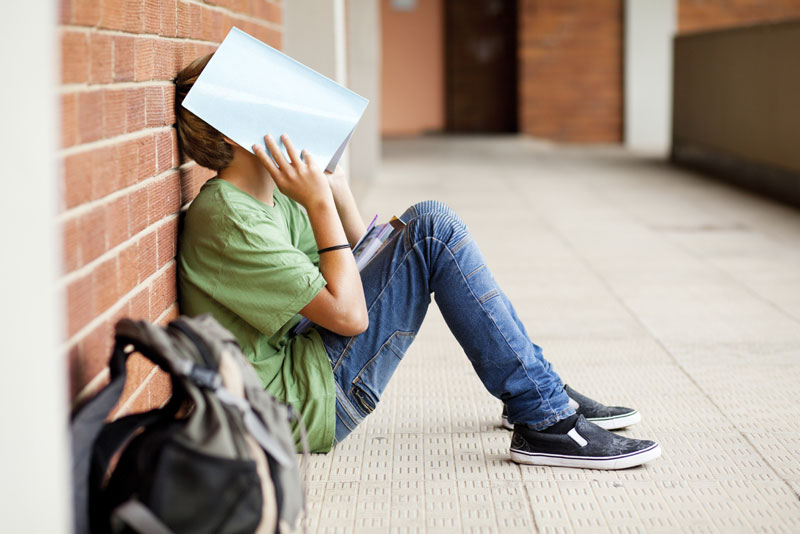 a student sitting on a floor with a book on face