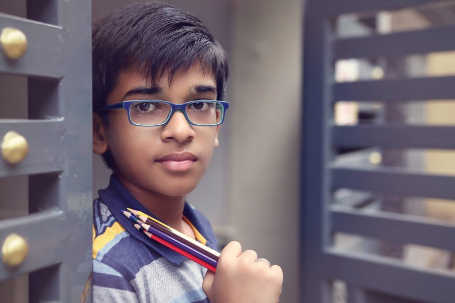 A young boy with glasses holding a pencil.