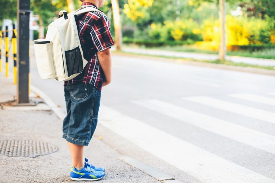 A boy with a backpack standing on a crosswalk.